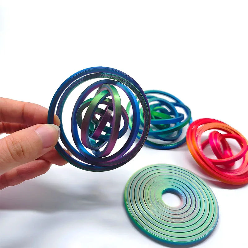 Hand holding a colorful rotating ball spinner fidget toy with various colored rings and a green disc.