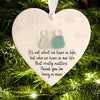 A white heart-shaped ornament with a frosted tree silhouette and two small figures, set against a green pine branch backgroun