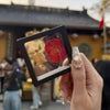 A hand holds a gold tortoise figurine for wealth luck home decor against a traditional building background.