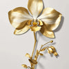 Flor de orquídea dorada y blanca con delicadas hojas doradas en una pared gris claro.