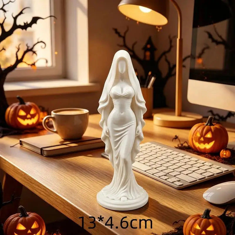 A white gold praying angel figurine statue displayed on a wooden table next to a laptop and pumpkins.