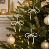 Elegant pearl bow Christmas tree ornaments hanging on a green fir branch.
