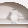 A white, ribbed ceramic vase is displayed on a shelf with dimension markings.