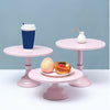A pink metal cake stand displaying a cup and a small vase on a white surface.