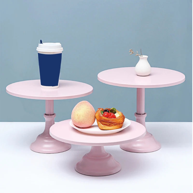 A pink metal cake stand displaying a cup and a small vase on a white surface.