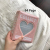 A pink 64 page collectible photo album with a heart cutout resting on white fabric.
