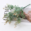 Green artificial fern and leaf sprigs arranged on a white card next to a hand.