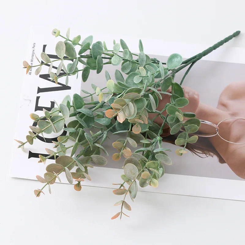 Green artificial fern and leaf sprigs arranged on a white card next to a hand.