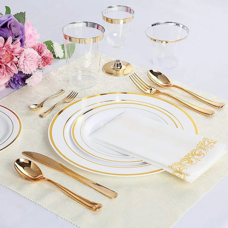 A set of gold disposable cutlery including forks, spoons, and knives arranged on a light fabric with clear glass cups.