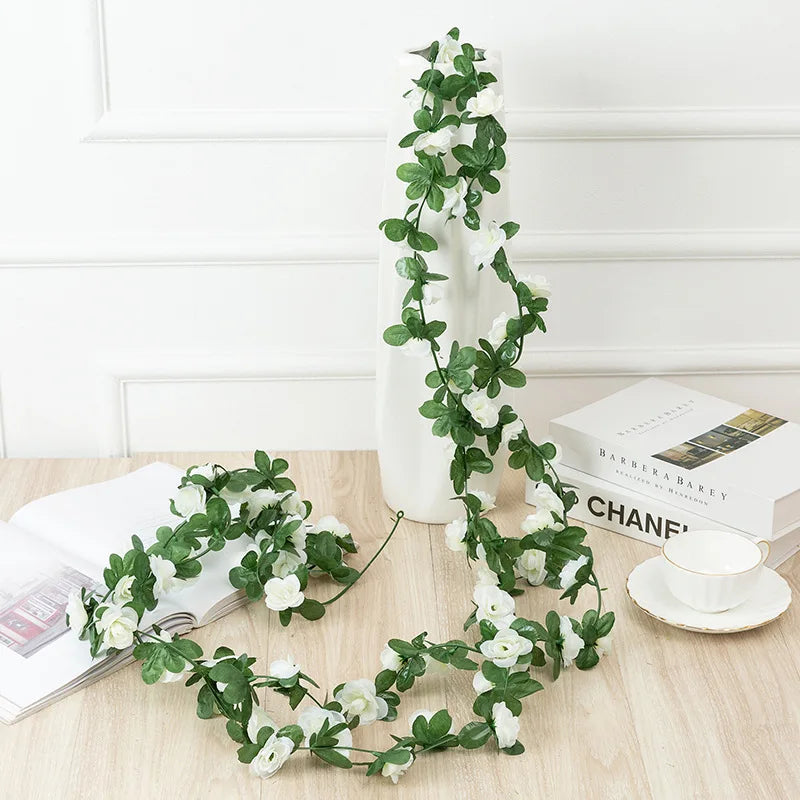A long green silk rose garland with white flowers draped vertically on a white vase.