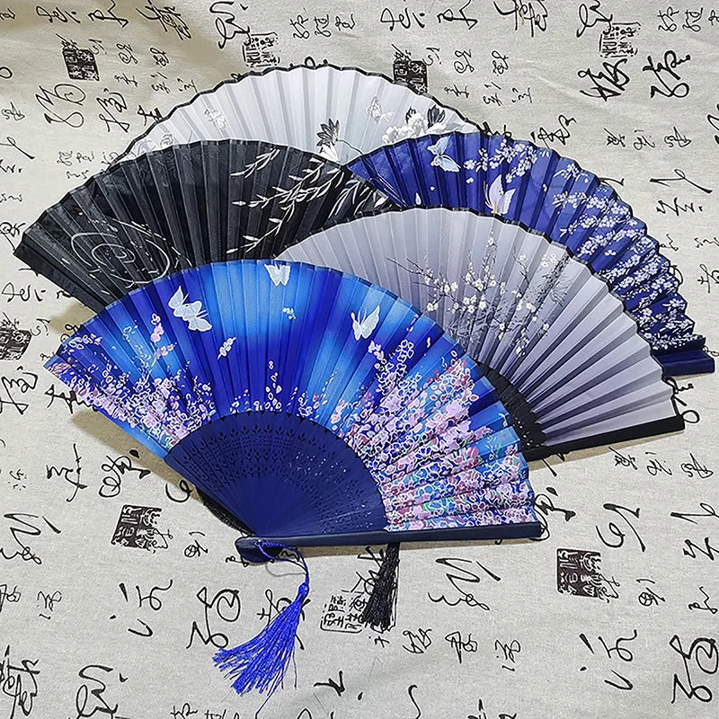 A collection of elegant vintage Chinese folding hand fans in various shades of blue and black displayed on a light patterned 