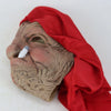 A realistic latex horror mask shaped like an elderly woman's face, covered by a flowing red fabric.