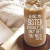 A clear tumbler filled with iced coffee sits on a wooden coaster next to a notebook.