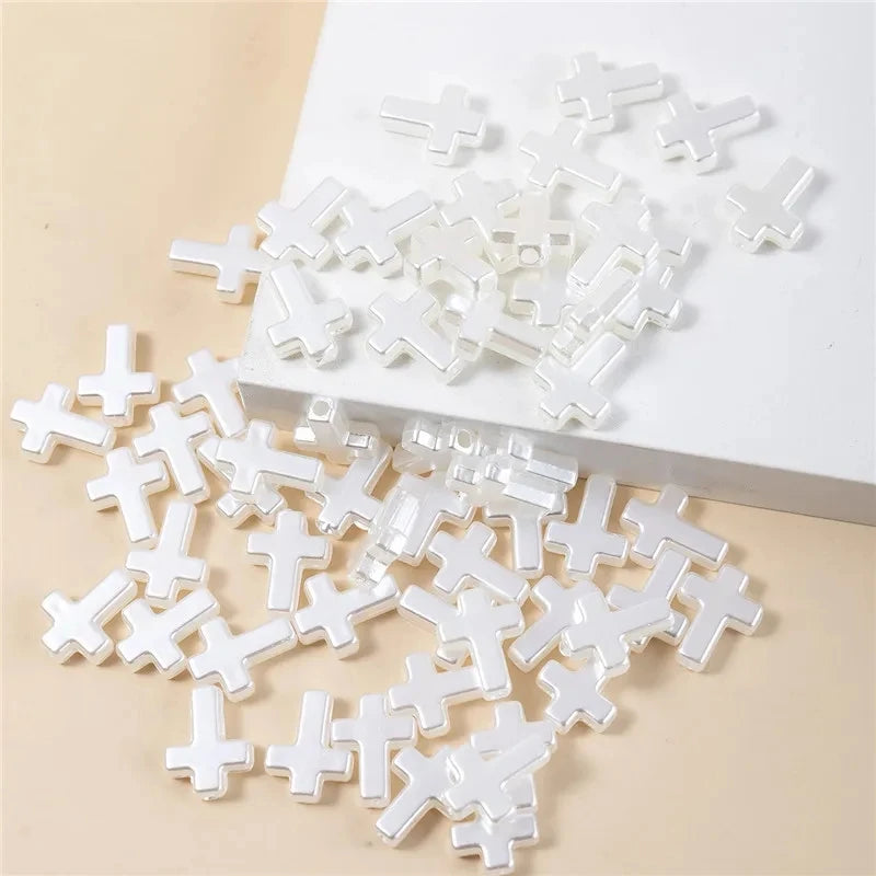 A pile of clear acrylic cross shape beads for DIY jewelry making on a white surface.