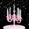 A pink candelabra holds nine white candles on a cake stand against a dark background with gold glitter.