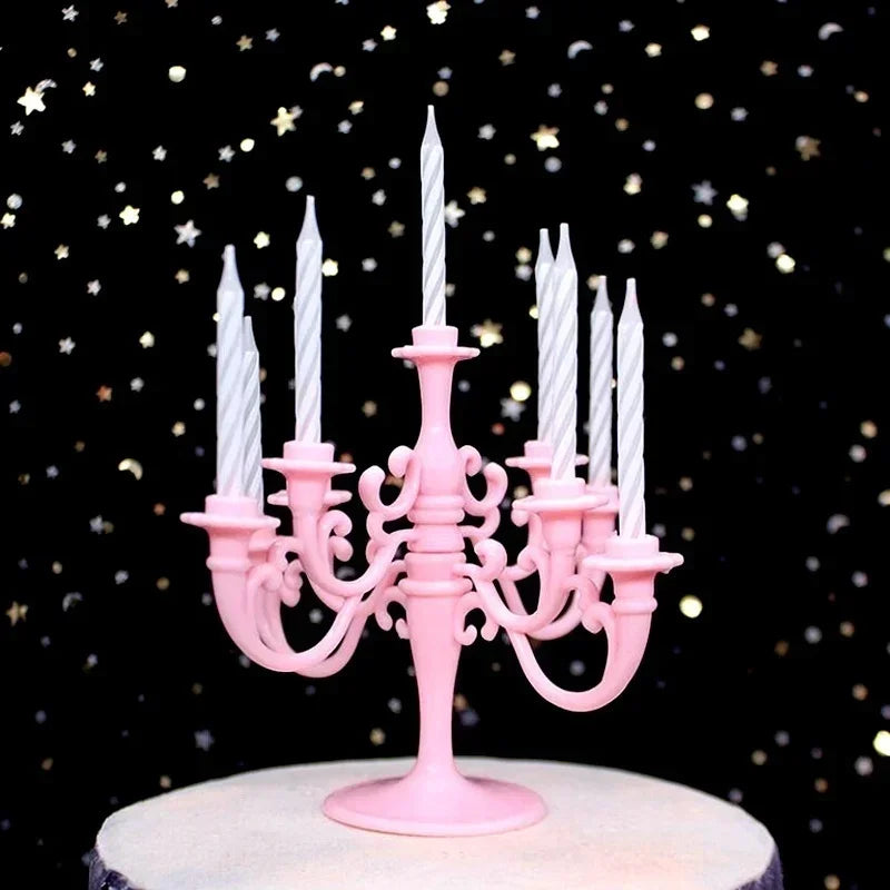 A pink candelabra holds nine white candles on a cake stand against a dark background with gold glitter.