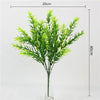 A tall glass vase filled with vibrant green artificial fern and leaf sprigs for home decor