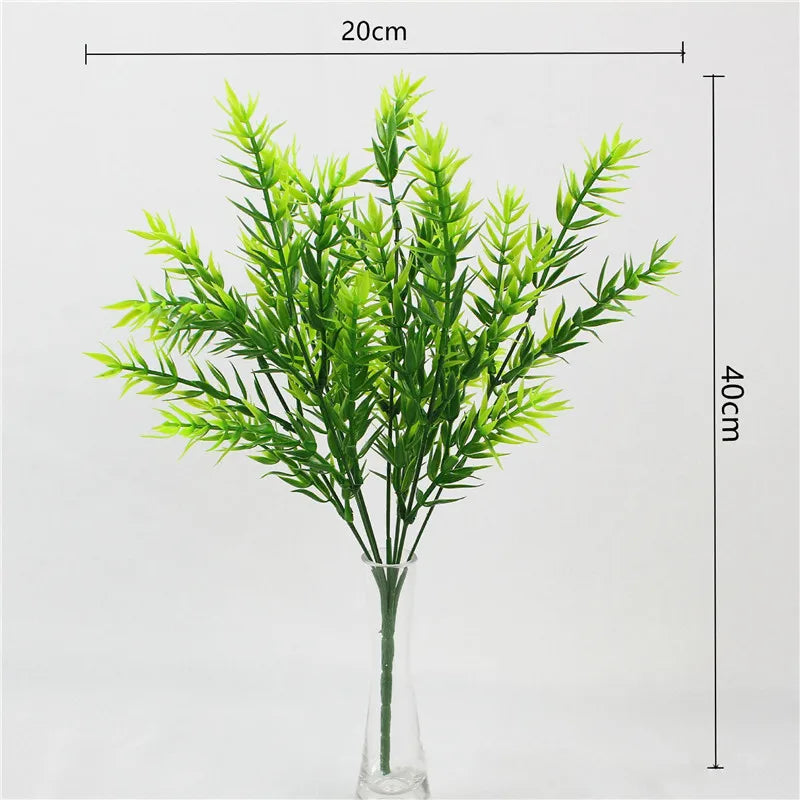 A tall glass vase filled with vibrant green artificial fern and leaf sprigs for home decor