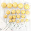 A set of twenty round, golden yellow ball cake toppers on thin green sticks.