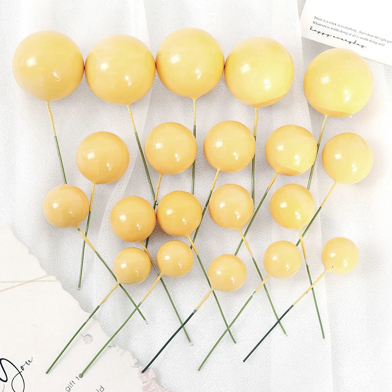 A set of twenty round, golden yellow ball cake toppers on thin green sticks.