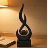 A black, stylized flame sculpture decor resting on a dark square base.