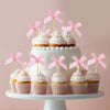 A tiered white cake decorated with pink buttercream frosting and pink bow toppers on a white stand.