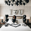 Un lit décoré de ballons en feuille noire et argent, en forme de lettres et de cœurs, avec un grand cœur au centre.