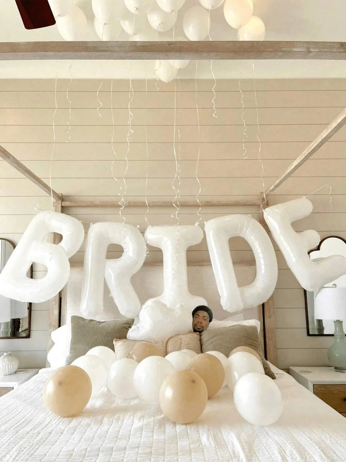 A display of white letter foil balloons spelling BRIDE hanging from a wooden frame against a light background.