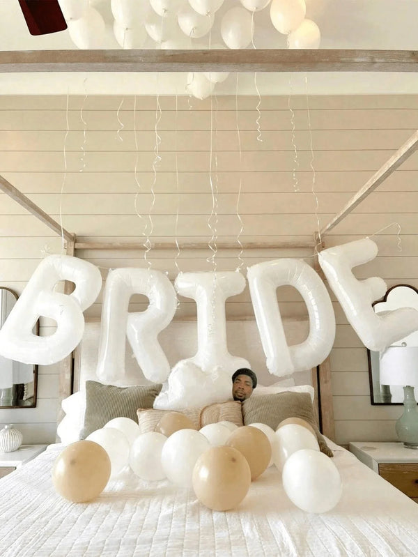 Affichage de ballons en feuille blanche formant le mot BRIDE, suspendus à un cadre en bois sur fond clair.