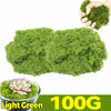A hand holds a clump of light green artificial moss, with a bowl of the same moss visible below.