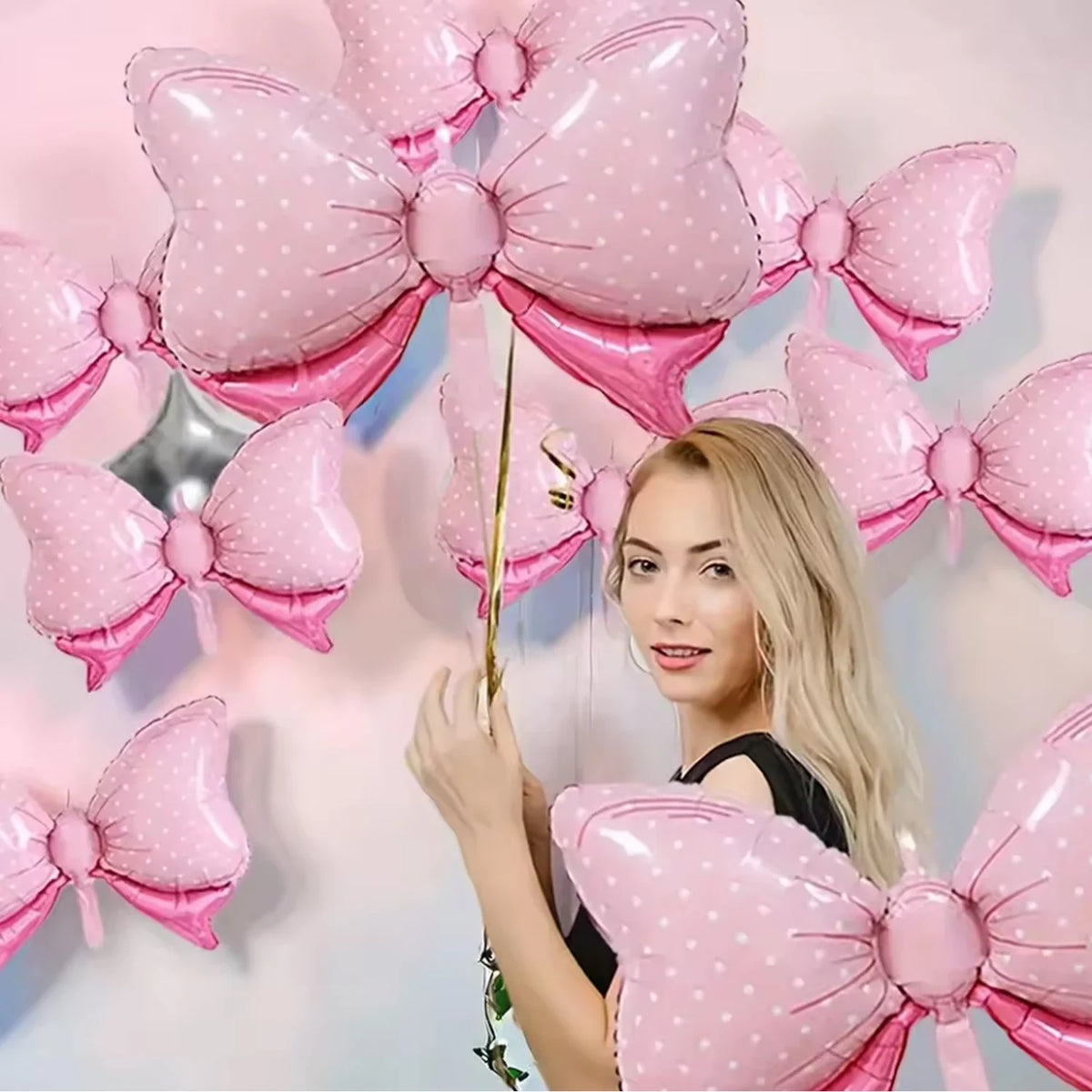 A woman holds a pink bow balloon decoration with white polka dots against a light background.