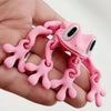 A hand holds a pink 3D frog fridge magnet with movable joints.