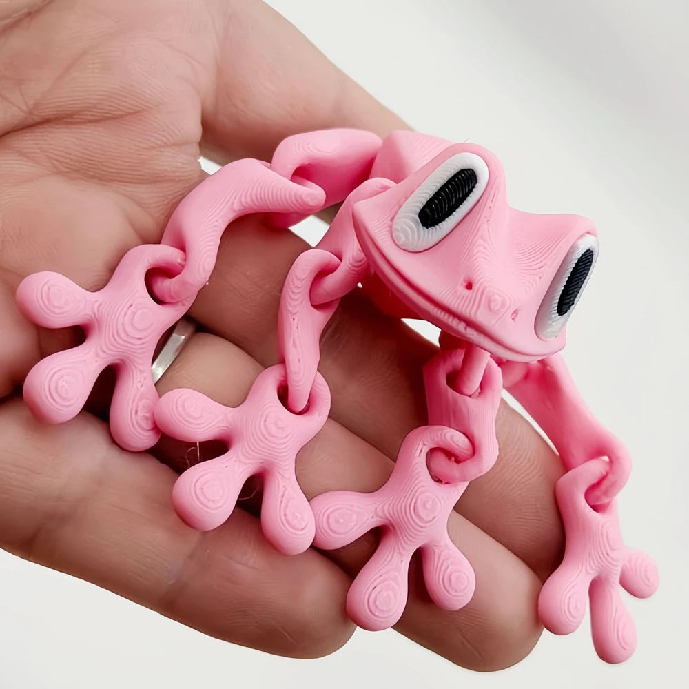 A hand holds a pink 3D frog fridge magnet with movable joints.