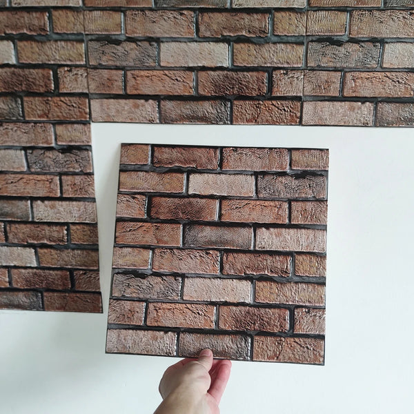 A close-up view of a rectangular brown brick pattern wall sticker being held up against a white background.