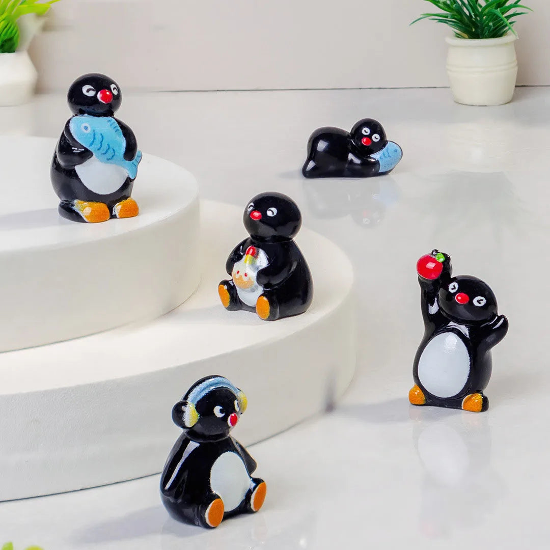 A collection of cute cartoon penguin resin figurines in black and white are displayed on a white surface.