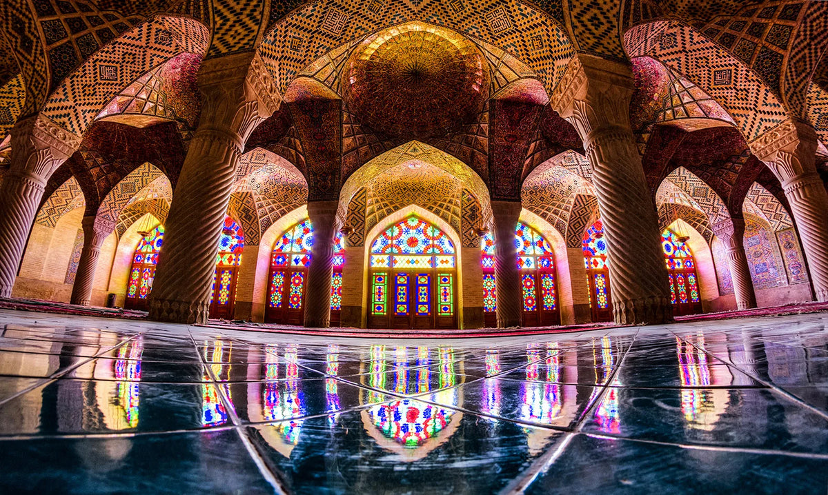 Interior view of an Islamic mosque with intricate dome architecture and colorful stained glass windows.