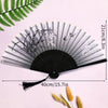Elegant black and white bamboo folding hand fan with a tassel displayed against a light pink background.