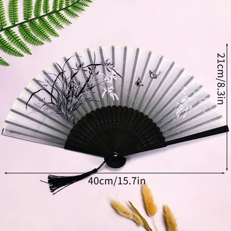 Elegant black and white bamboo folding hand fan with a tassel displayed against a light pink background.