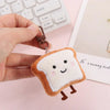 A fluffy toast bread plush charm with brown edges and small pink eyes is being held by a hand against a white background.