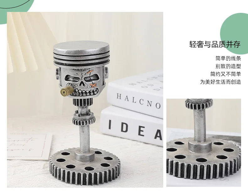 A silver mechanical piston skull sculpture with a gear base and piston rod, displayed on a white surface.