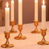 A row of tall white candles in vintage gold iron candlestick holders on a light surface.