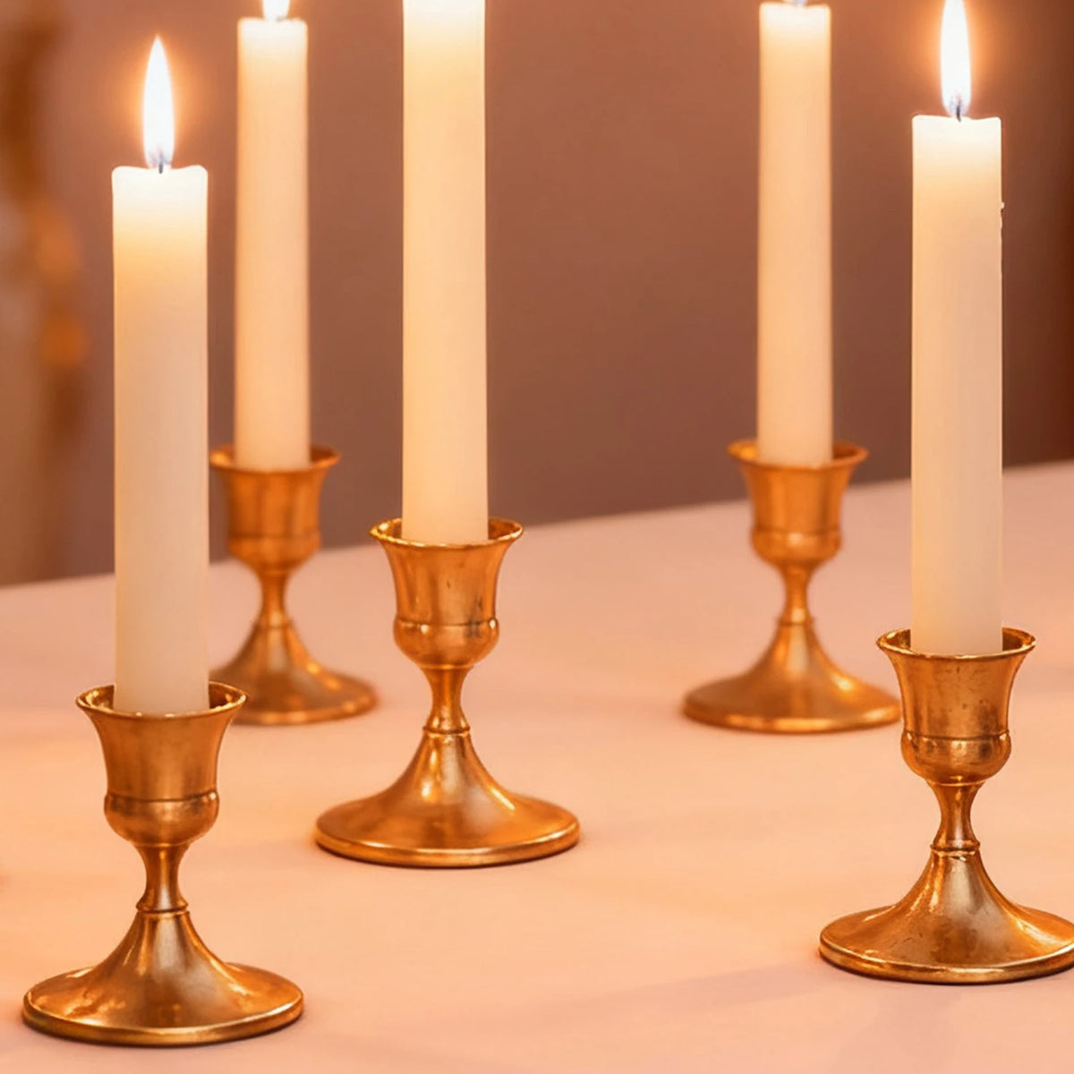 A row of tall white candles in vintage gold iron candlestick holders on a light surface.