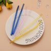 A collection of colorful reusable borosilicate glass straws with cleaning brushes arranged on a white plate.