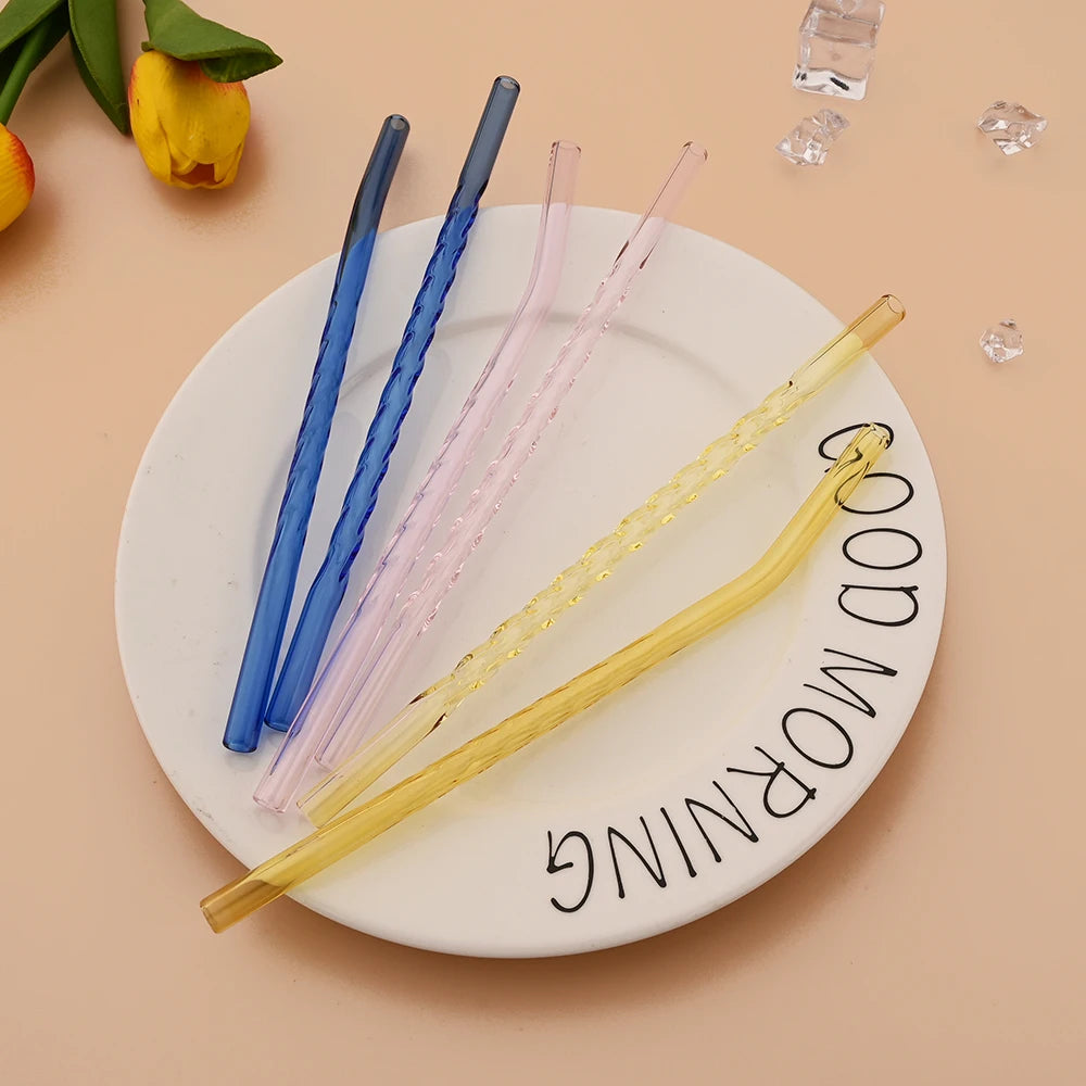 A collection of colorful reusable borosilicate glass straws with cleaning brushes arranged on a white plate.