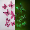 A set of twelve 3D luminous butterfly wall stickers in pink and green colors.