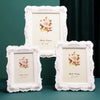 Three white ornate photo frames with floral accents displayed on a dark green surface.