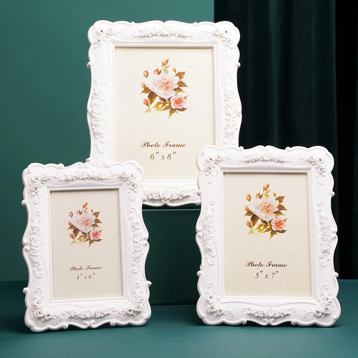 Three white ornate photo frames with floral accents displayed on a dark green surface.
