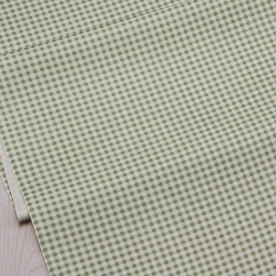 A close-up view of light green fabric with a repeating small floral pattern for sewing and quilting.
