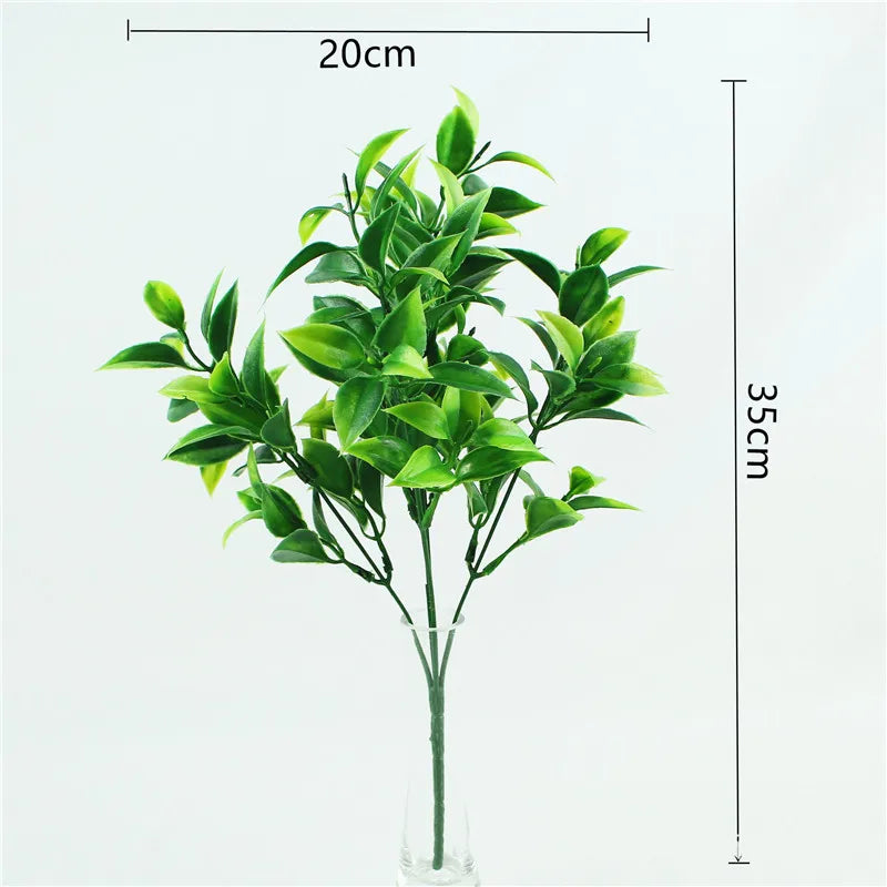 A sprig of green artificial fern and leaf branches displayed in a clear glass vase.