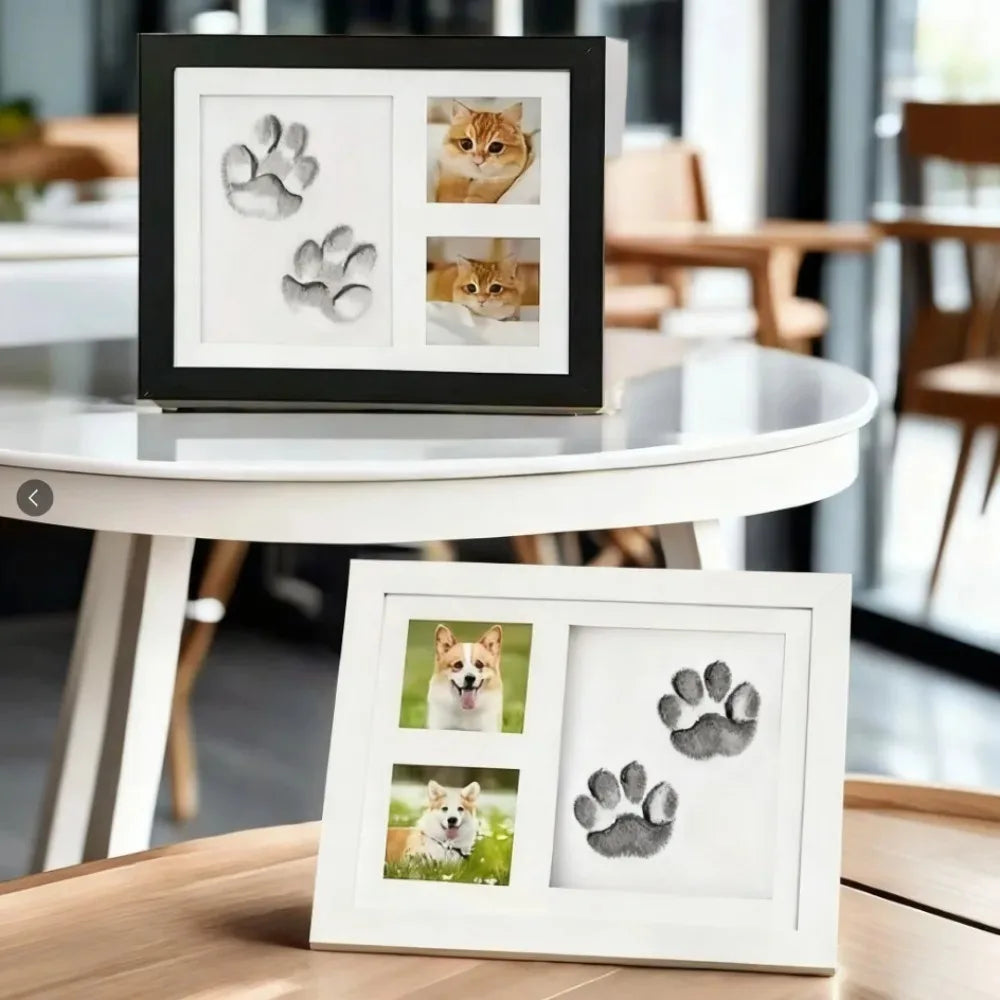 A black photo frame displaying clay paw prints and a cat's face, set on a round white table.
